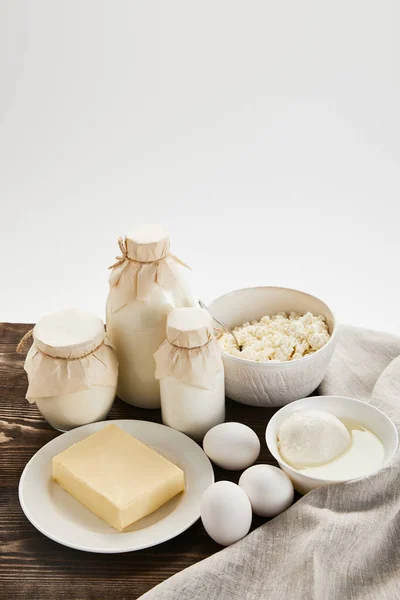 Deliciosos productos lácteos frescos y huevos en mesa de madera rústica con tela aislada en blanco - foto de stock