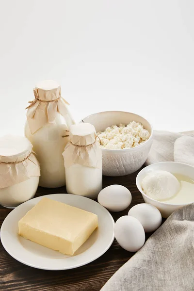 Deliciosos produtos lácteos frescos e ovos em mesa de madeira rústica com pano isolado em branco — Fotografia de Stock
