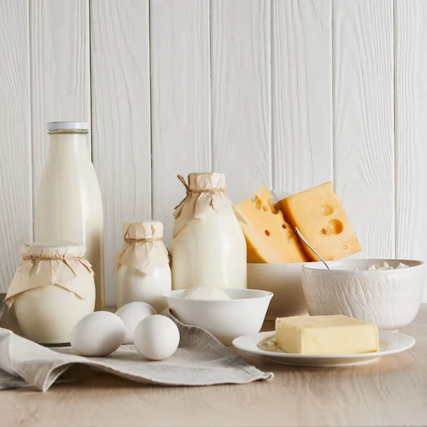 Deliciosos produtos lácteos frescos e ovos em fundo de madeira branca — Fotografia de Stock