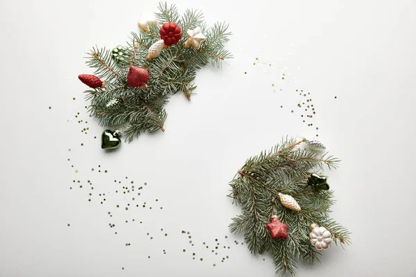 Верхний вид праздничного Рождества украшенные сосновые ветви с безделушками и конфетти на белом фоне — стоковое фото