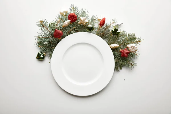 Top view of white plate near festive Christmas tree branch with baubles on white background — Stock Photo