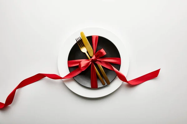 Top view of white and black plates with cutlery and ribbon on white background — Stock Photo