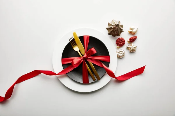 Top view of white and black plates with cutlery and ribbon near festive Christmas baubles on white background — Stock Photo