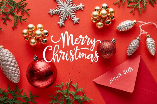 Vista superior de la decoración de Navidad brillante, sobre y thuja sobre fondo rojo con ilustración de Feliz Navidad — Stock Photo