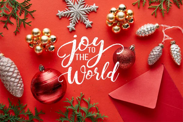 Vista superior de brillante decoración de Navidad, sobre y thuja sobre fondo rojo con alegría a la ilustración del mundo - foto de stock