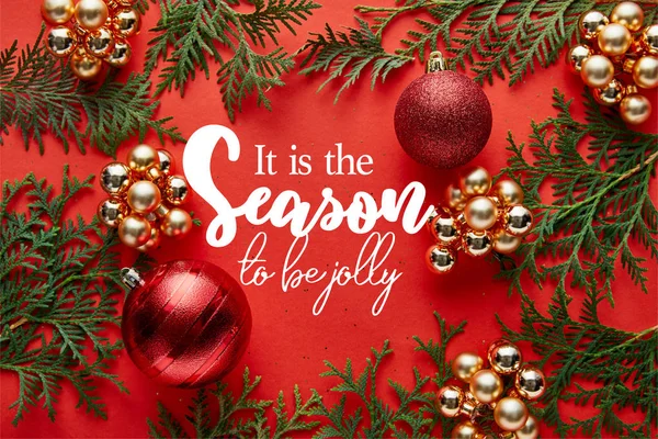 Vista superior de la decoración brillante de Navidad y thuja sobre fondo rojo con él es la temporada para ser letras alegres - foto de stock