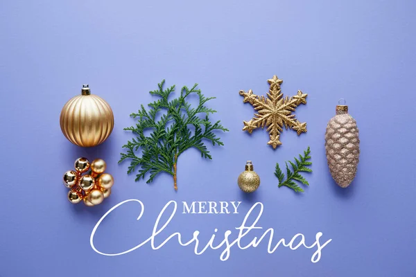 Верхний вид блестящего золотого рождественского украшения, зеленые ветви туи на синем фоне с весёлой рождественской иллюстрацией — стоковое фото