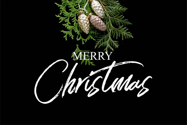 Vista superior de brillantes conos dorados de Navidad en ramas de thuja verdes aisladas en negro con ilustración de Feliz Navidad - foto de stock