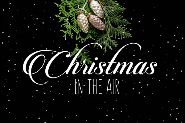 Vista superior de brillantes conos dorados de Navidad en ramas de thuja verdes aisladas en negro con ilustración de Navidad en el aire - foto de stock
