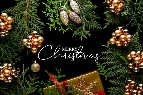 Top view of shiny golden Christmas decoration, green thuja branches and gift box isolated on black with Merry Christmas illustration — Stock Photo