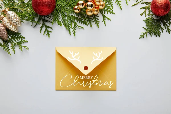 Vista superior da decoração dourada brilhante do Natal e envelope com ilustração Feliz Natal perto de ramos thuja verdes isolados no branco — Fotografia de Stock