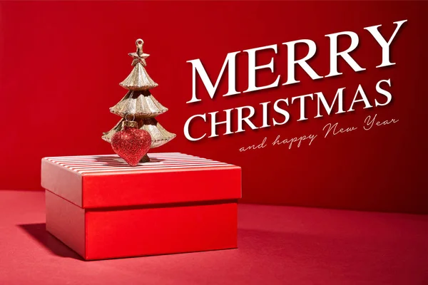 Boîte cadeau rouge rayé et arbre de Noël doré décoratif avec boule sur fond rouge avec Joyeux Noël et heureuse illustration de nouvelle année — Stock Photo