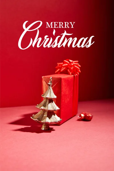 Caja de regalo roja y árbol de Navidad dorado decorativo con adorno sobre fondo rojo con ilustración de Feliz Navidad - foto de stock