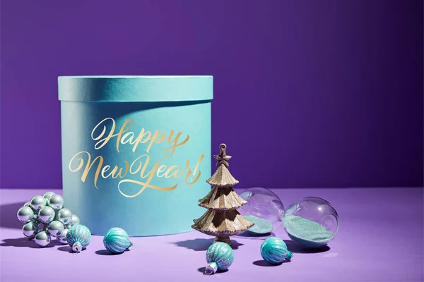 Caja de regalo azul y árbol de Navidad decorativo con adornos sobre fondo púrpura con letras feliz año nuevo - foto de stock