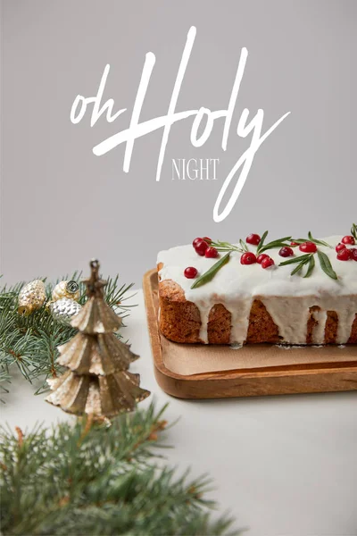 Traditional Christmas cake with cranberry near baubles and pine on white table isolated on grey with o holy night illustration — Stock Photo