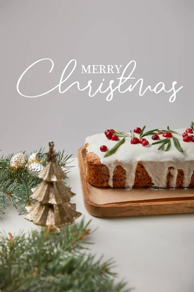 Traditional Christmas cake with cranberry near baubles and pine on white table isolated on grey with Merry Christmas illustration — Stock Photo