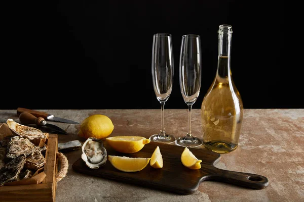 Deliziose ostriche vicino limoni e bottiglia con spumante isolato su nero — Foto stock