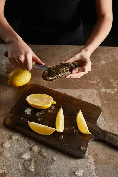 Vue recadrée d'une femme tenant un couteau lors de l'ouverture d'une huître près de citrons — Photo de stock