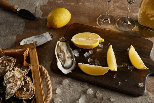Deliciosas ostras perto de limões e gelo derretendo na placa de corte de madeira — Fotografia de Stock