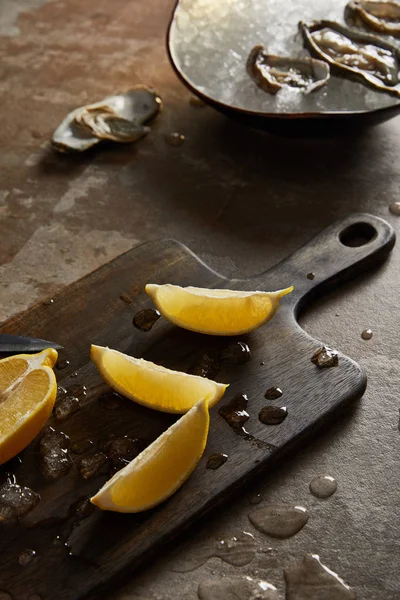 Concentrazione selettiva di limoni freschi sul tagliere vicino alle ostriche in ciotola con cubetti di ghiaccio — Foto stock