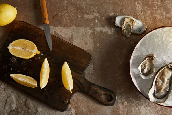 Top view of fresh lemons on cutting board near oysters in bowl with ice cubes — Stock Photo