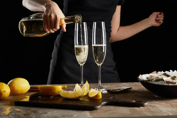 Cropped view of woman pouring sparkling wine in champagne glass near oysters in bowl with ice isolated on black — Stock Photo