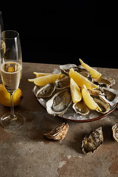 Champagne glass with sparkling wine near oysters and lemons in bowl isolated on black — Stock Photo