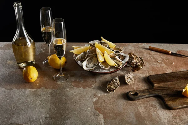 Champagne glasses with sparkling wine near bottle, oysters and lemons in bowl isolated on black — Stock Photo