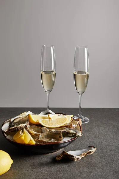 Champagne glasses with sparkling wine near delicious oysters and lemons in bowl isolated on grey — Stock Photo