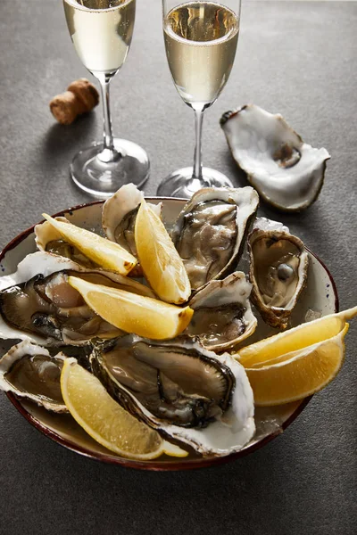 Foyer sélectif de délicieuses huîtres et citrons dans un bol près de verres à champagne avec du vin mousseux sur la surface grise — Photo de stock