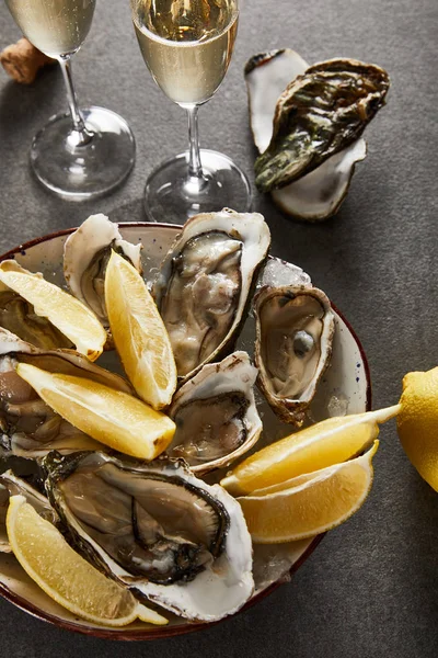 Vista superior de deliciosas ostras e limões na tigela perto de taças de champanhe com vinho espumante na superfície cinza — Fotografia de Stock