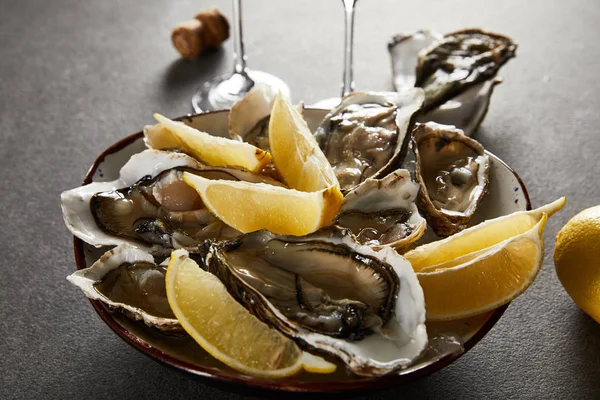 Selective focus of tasty oysters and lemons in bowl with ice on grey surface — Stock Photo