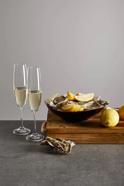 Delicious oysters and lemons in bowl near champagne glasses with sparkling wine isolated on grey — Stock Photo