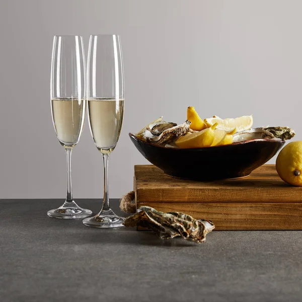 Huîtres fraîches et citrons dans un bol près de verres à champagne avec vin mousseux isolé sur gris — Photo de stock