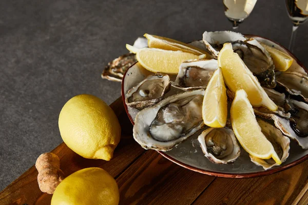 Enfoque selectivo de limones enteros cerca de ostras en tazón y copas de champán en superficie gris - foto de stock