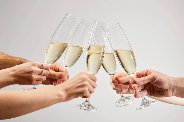 Обрезанный вид мужчин и женщин, звонящих бокалы шампанского с игристым вином изолированы на сером — стоковое фото