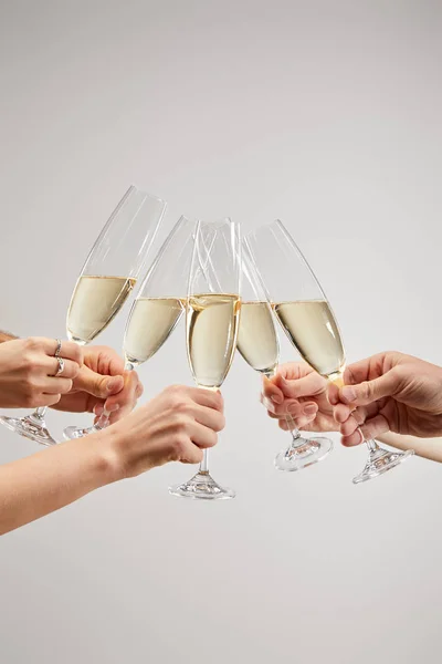 Vista recortada de mujeres y hombres brindar copas de champán con vino espumoso aislado en gris - foto de stock