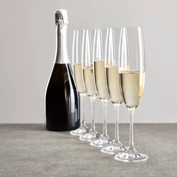 Selective focus of champagne glasses with sparkling wine near bottle isolated on grey — Stock Photo