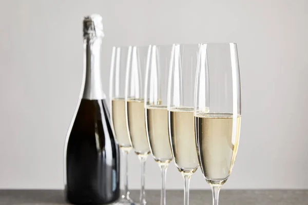 Foco seletivo de vinho espumante em copos de champanhe perto de garrafa isolada em cinza — Fotografia de Stock