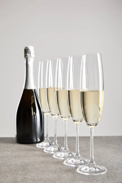 Selective focus of sparkling wine in champagne glasses near bottle on surface isolated on grey — Stock Photo