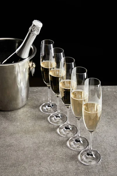 Champagne glasses with sparkling wine near bottle in ice bucket isolated on black — Stock Photo