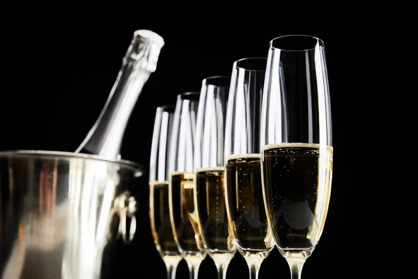 Enfoque selectivo de copas de champán con vino espumoso cerca de cubo de hielo con botella aislada en negro - foto de stock