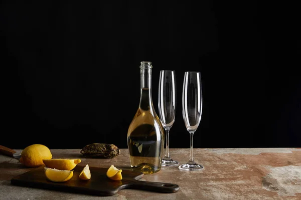 Deliciosa ostra en cáscara cerca de limones y botella con vino espumoso aislado en negro - foto de stock