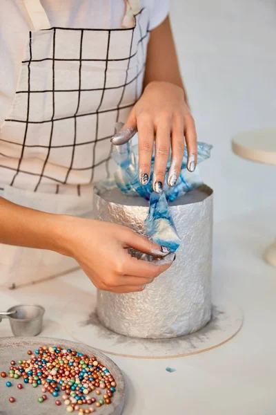 Cropped view of confectioner decorating cake on kitchen table — Stock Photo