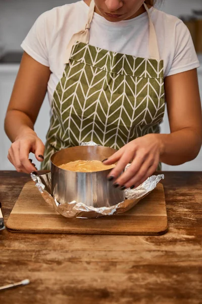 Vista ritagliata del pasticciere in piedi vicino torta al forno in stampo torta su lamina di metallo su tavolo di legno — Foto stock