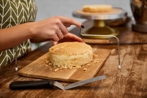 Vista cortada de bolo de corte de confeiteiro com cortador de bolo na tábua de corte — Fotografia de Stock