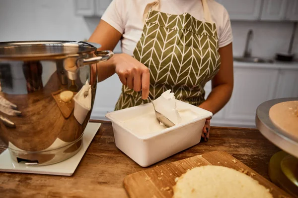 Teilansicht des Konditors, der Sahne aus Behälter nimmt, um Kuchen zu kochen — Stockfoto