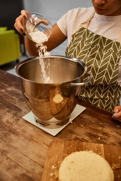 Vista cortada de confeiteiro adicionando farinha na tigela ao lado da camada de biscoito na placa de corte — Fotografia de Stock