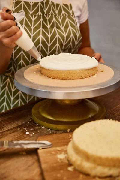 Vista recortada del pastelero poniendo crema de la bolsa de pastelería en la torta de esponja - foto de stock