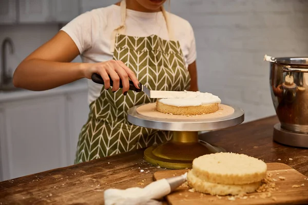 Vista ritagliata del pasticciere che mette la crema con spatola su strato di torta — Foto stock